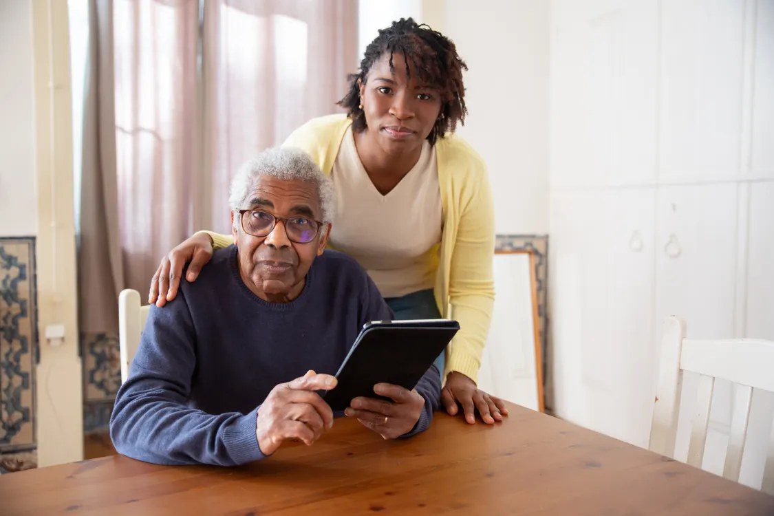 A senior man and a caregiver looking at a tablet together at home